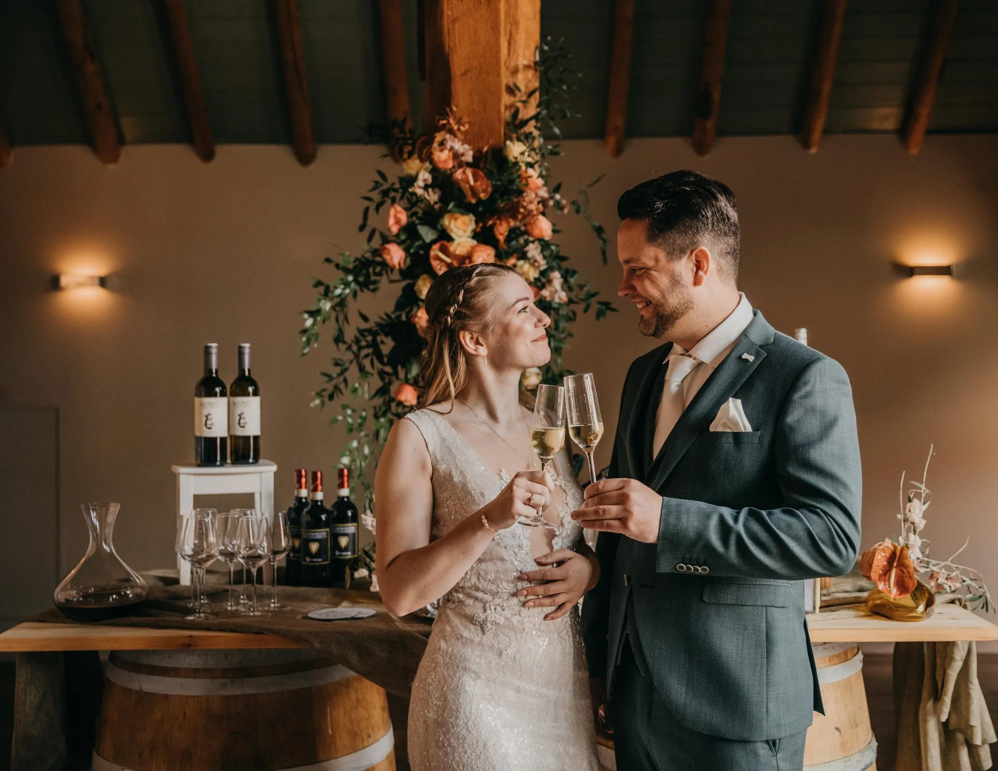 Bruidspaar proost met champagne bij een bloemenboog